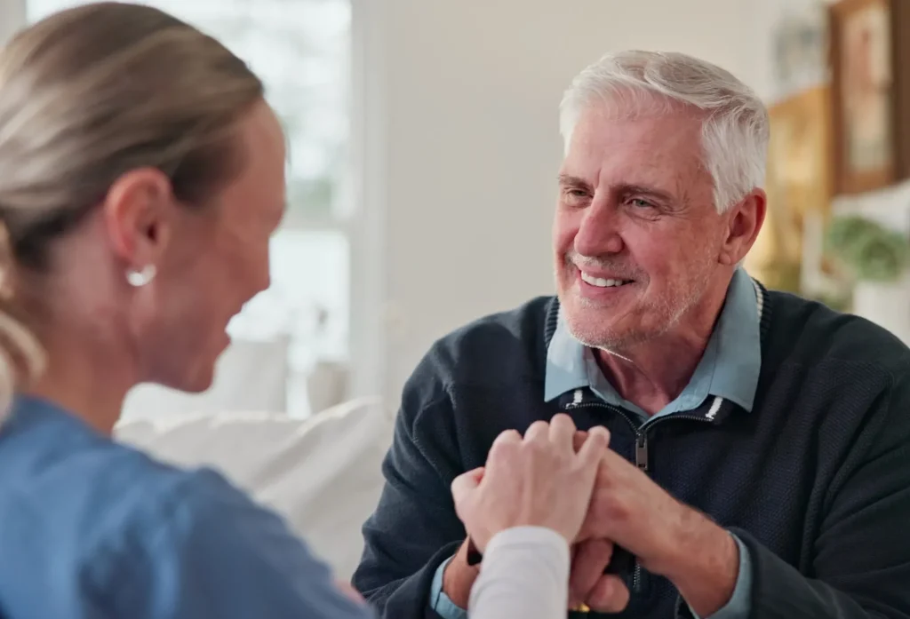 Elderly man holding hands with a caregiver at home